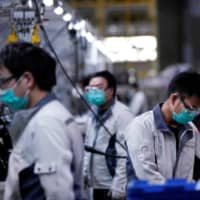 Employees wearing masks work on a car seat assembly line at the Yanfeng Adient factory in Shanghai on Feb. 24. | REUTERS