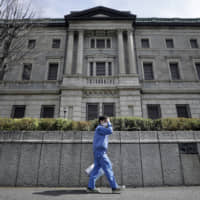 A pedestrian wearing a protective mask walks past Bank of Japan headquarters in Tokyo last Monday. | BLOOMBERG