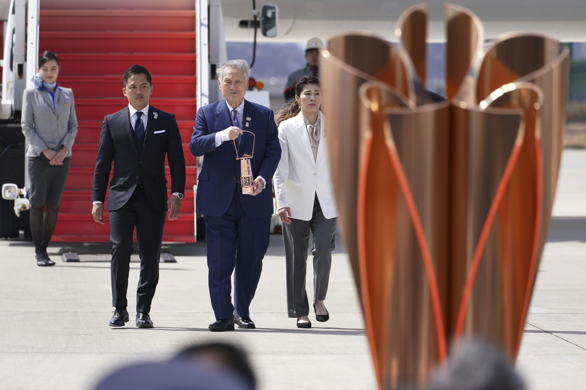 Tokyo 2020 Olympics chief Yoshiro Mori (third from left), followed by three-time Olympic gold medalists Tadahiro Nomura and Saori Yoshida, carries the Olympic flame during the arrival ceremony at Japan Air Self-Defense Force Matsushima Base in Higashimatsushima in Miyagi Prefecture on Friday. | AP