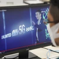 A monitor shows KDDI Corp. President Makoto Takahashi giving a presentation on the company\'s 5G wireless services during a teleconference Monday. | ?¯