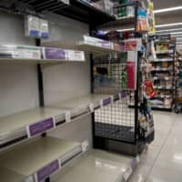 A masked employee works near shelves emptied by panic-buying of toilet paper and tissues at a supermarket in Tokyo on Wednesday. | REUTERS