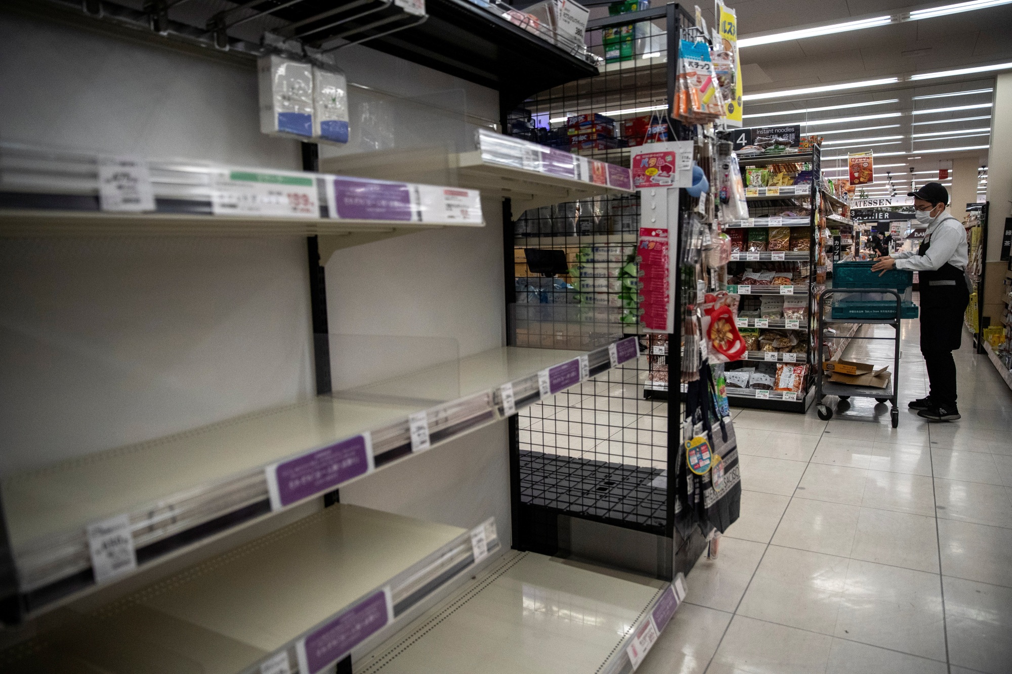 A masked employee works near shelves emptied by panic-buying of toilet paper and tissues at a supermarket in Tokyo on Wednesday. | REUTERS