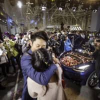 A Tesla employee kisses his girlfriend after proposing with his newly delivered Model 3 during a ceremony at the company\'s Gigafactory in Shanghai on Dec. 30, the first day Tesla Inc. delivered China-built cars. | BLOOMBERG