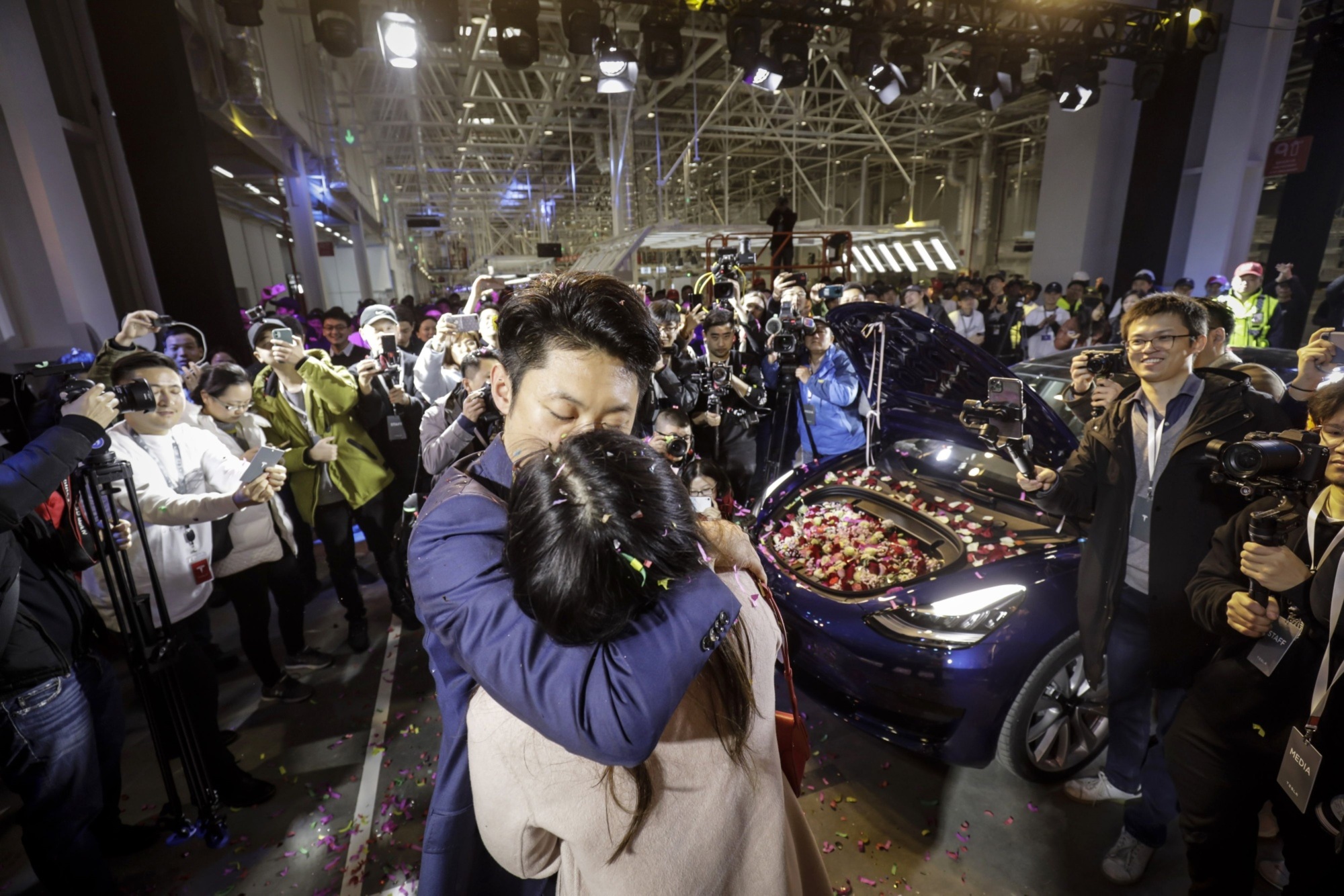 A Tesla employee kisses his girlfriend after proposing with his newly delivered Model 3 during a ceremony at the company's Gigafactory in Shanghai on Dec. 30, the first day Tesla Inc. delivered China-built cars. | BLOOMBERG