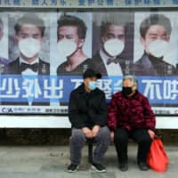 A man and woman sit in front of a poster reminding citizens to wear face masks as a preventive measure against the COVID-19 coronavirus, at a bus stop in Bozhou, in China\'s eastern Anhui province, on Friday. | AFP-JIJI