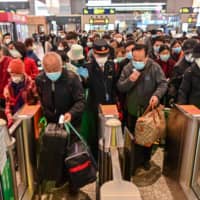 People wearing face masks as a preventive measure against the COVID-19 novel coronavirus walk to a train, one of the stops being Wuhan, at a station in Shanghai on Saturday. | AFP-JIJI