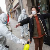 A woman who has recovered from the COVID-19 coronavirus infection is disinfected by volunteers as she arrives at a hotel for a 14-day quarantine after being discharged from a hospital in Wuhan, in China\'s central Hubei province, on Sunday. | AFP-JIJI
