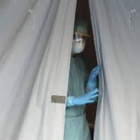 A medical staffer watches from a tent Thursday at one of the emergency structures that were set up to ease procedures at the Brescia hospital in northern Italy. | AP