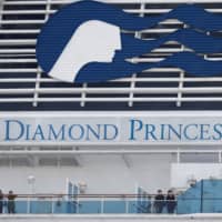 Masked passengers look on from aboard the coronavirus-hit Diamond Princess cruise ship docked at Yokohama on Feb. 20. | REUTERS
