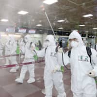 South Korean soldiers wearing protective gear spray disinfectant to help prevent the spread of the COVID-19 coronavirus, at Daegu International Airport in Daegu on Friday. | YONHAP / VIA AFP-JIJI