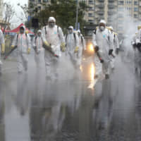 Taiwanese Army soldiers wearing protective suits spray disinfectant over a road during a drill to prevent community cluster infection, in New Taipei City on Saturday. | AP