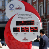 Passersby take pictures of an Olympics countdown clock in front of Tokyo Station Wednesday as it stopped displaying the number of days until the games, a day after Prime Minister Shinzo Abe announced the games will be postponed. | YOSHIAKI MIURA
