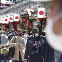 Visitors wearing face masks walk through Nakamise alley at Tokyo\'s Asakusa district on Friday. | AP