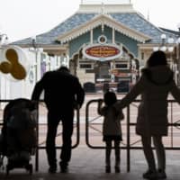 A family looks at the shuttered entrance of Tokyo Disneyland near Tokyo on Feb. 29 due to a closure in the wake of the coronavirus outbreak. | KYODO