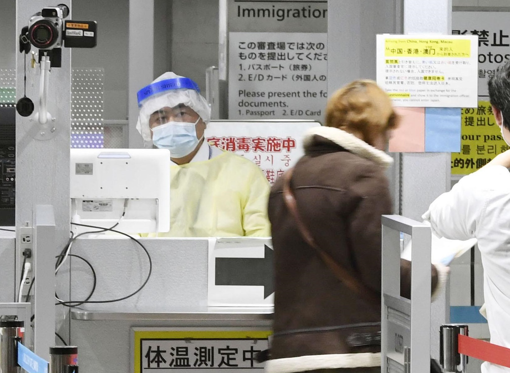 A quarantine officer in protective gear at Narita International Airport performs checks on people arriving from South Korea on Monday morning. | KYODO