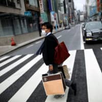 A man wearing a protective face mask walks in the Ginza shopping district in Tokyo on Saturday. | REUTERS