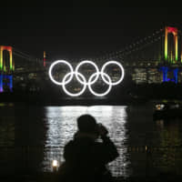 A photographer takes pictures of the illuminated Olympic rings in front of the Rainbow Bridge in Tokyo\'s Odaiba area on Jan. 24. | AP