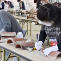 Volunteers remove plaster from roof tiles taken from the burned-out remains of Shuri Castle in Naha on Monday so they can be reused in the landmark\'s restoration. | KYODO