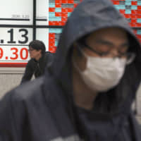 People walk in the rain past an electronic stock board showing Japan\'s Nikkei 225 index at a securities firm in Tokyo on Monday. | AP