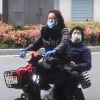 Women wearing face masks ride a scooter on a street in Wuhan,  China — the epicenter of the coronavirus outbreak — on Saturday after travel restrictions into the city were eased following two months of lockdown due to the COVID-19 pandemic. | AFP-JIJI