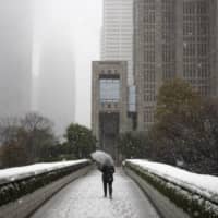 A solitary individual walks along a bridge as snow falls Sunday in Tokyo. Gov. Yuriko Koike has asked the city\'s 13 million residents to stay home this weekend, saying the capital is on the brink of an explosion in coronavirus infections. | AP