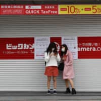 Women wearing masks stand in front of a shuttered electronics store in Tokyo on Saturday. | BLOOMBERG