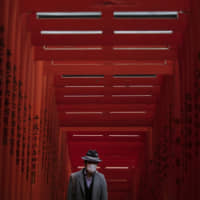 Social distance: A man wearing a mask walks through torii gates at Tokyo\'s Hie Shrine. As the new coronavirus, officially known as COVID-19, began to spread, panic buying resulted in shortages of masks and toilet paper throughout Japan. | AP