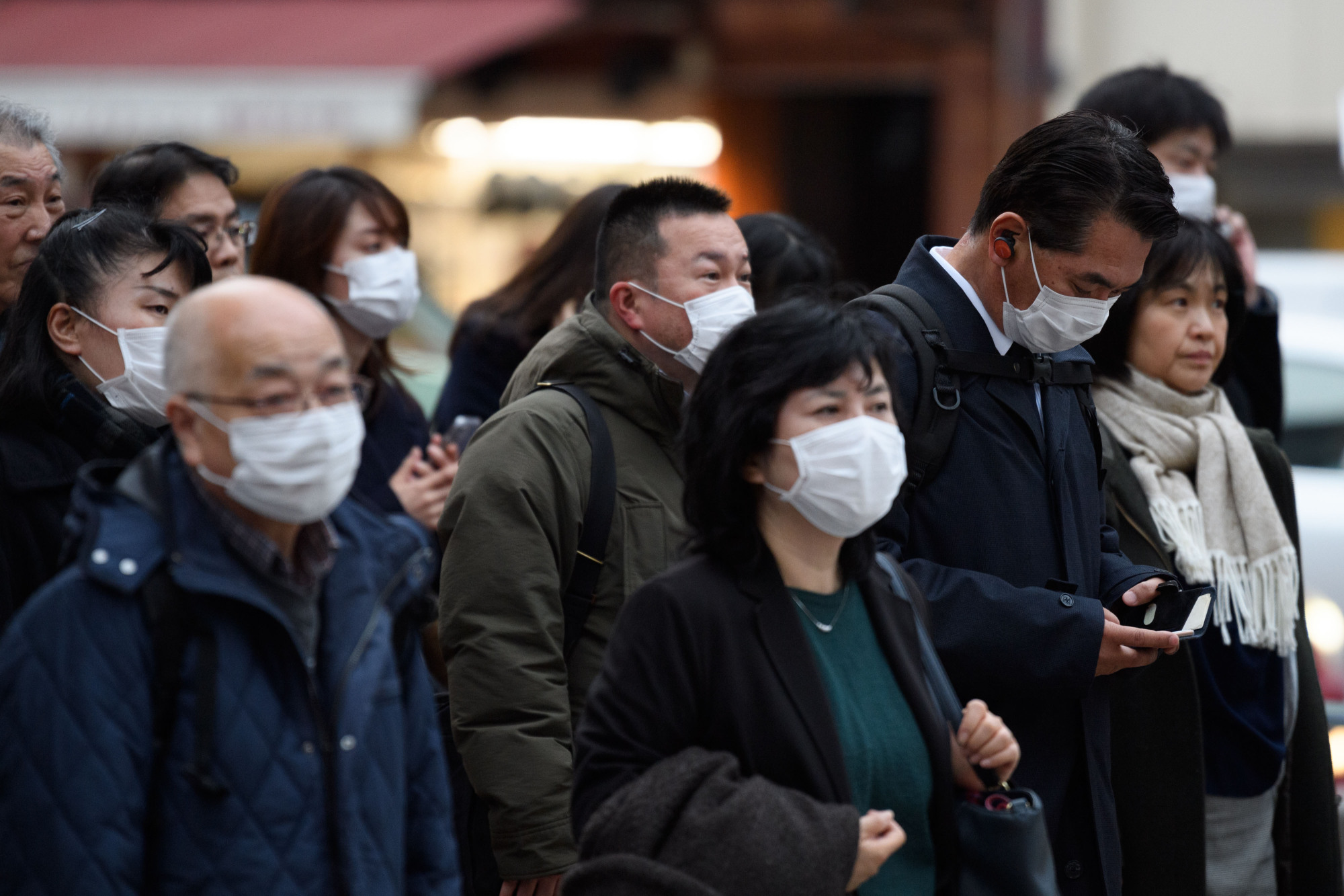 Pedestrians wearing protective masks wait to cross a road in Tokyo on Monday. The government must disseminate more  information on the outbreak in foreign languages. | BLOOMBERG