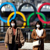 Women wearing face masks to help prevent coronavirus infection walk in the waterfront area at Odaiba Marine Park in Tokyo on Feb. 27. | REUTERS