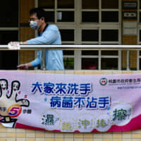 A man cleans a handrail at a middle school in Taoyuan, northern Taiwan, on Saturday behind a sign telling students how to wash their hands to prevent the transmission of COVID-19. | AFP-JIJI