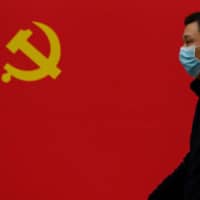 A man walks past a Communist Party flag along a street in Wuhan, China on Tuesday.  | AFP-JIJI