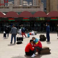 People wait outside Beijing Railway Station on Wednesday as the spread of COVID-19 continues.  | REUTERS