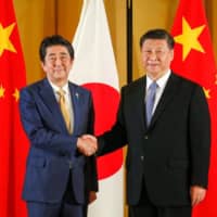 Prime Minister Shinzo Abe shakes hands with Chinese President Xi Jinping during a bilateral meeting ahead of the Group of 20 summit in Osaka last June. Abe has refrained from blaming China for the COVID-19 crisis. | BLOOMBERG
