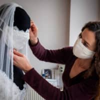 Clothing designer Friederike Jorzig adjusts a mannequin wearing a wedding dress with matching protective mask in her store Chiton in Berlin on Tuesday. | AFP-JIJI