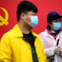 People stand in front of a Communist Party of China flag along a street in Wuhan, China, on Thursday.  | AFP-JIJI