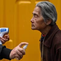 An elderly woman is sprayed with disinfectant by a volunteer at the entrance to a neighborhood in Wuhan on Thursday.  | AFP-JIJI