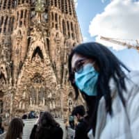Before lockdown: A tourist wears a protective face mask at the Sagrada Familia cathedral in Barcelona early last month. | BLOOMBERG