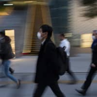 Commuters walk along a sidewalk Monday in Tokyo. | AP