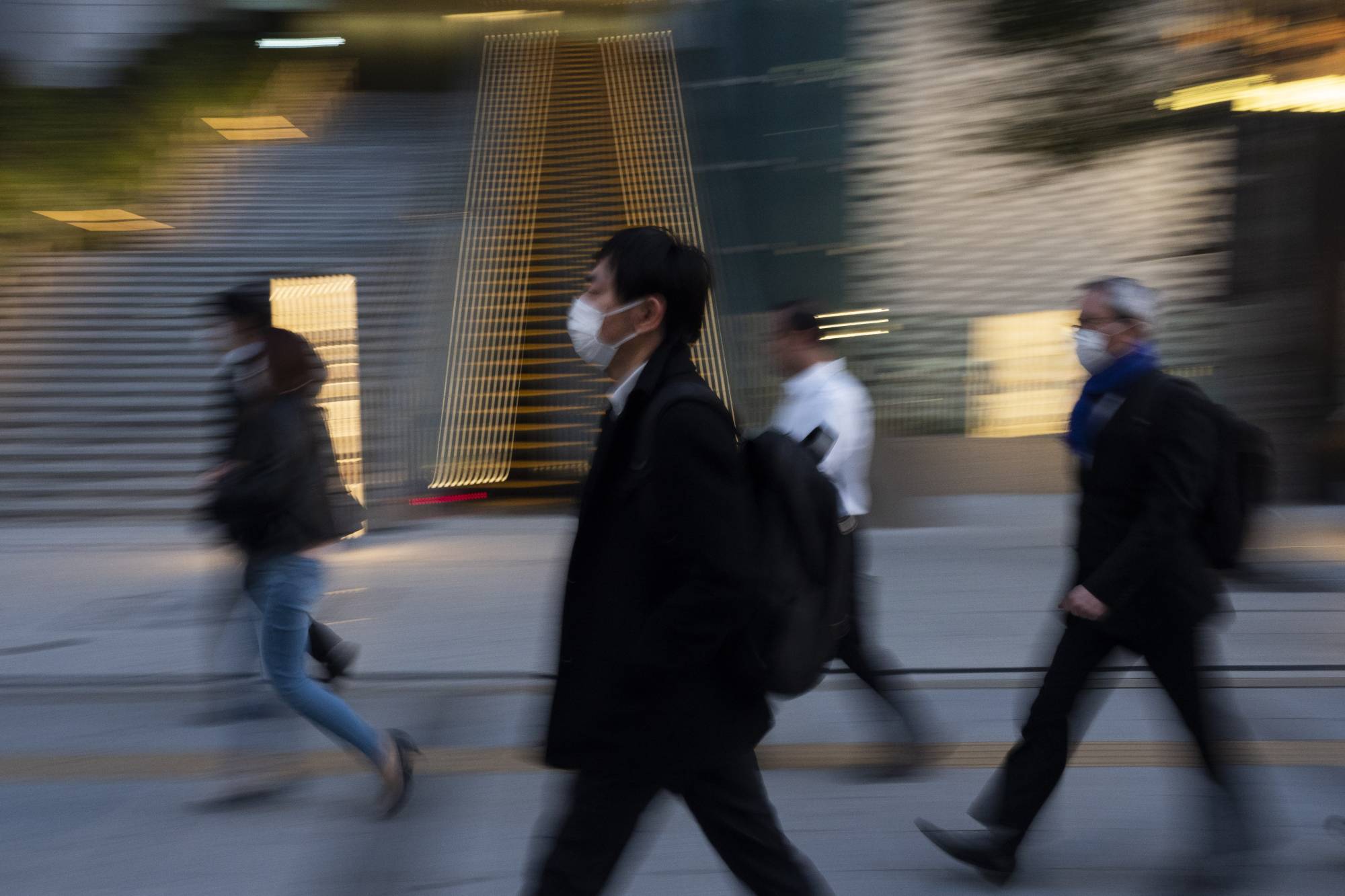 Commuters walk along a sidewalk Monday in Tokyo. | AP