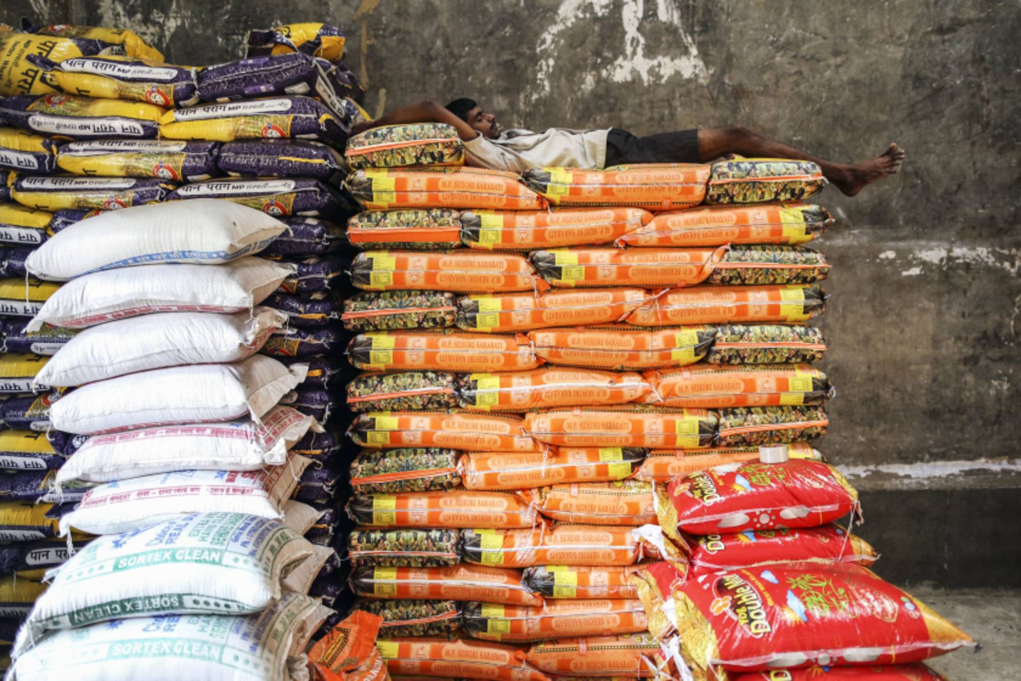 A worker sleeps on bags of wheat during a break at a wholesale market in Mumbai, India, last month. | BLOOMBERG