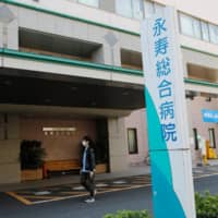 A man wearing a protective face mask walks in front of Eiju General Hospital, where more than 100 people have been infected with the coronavirus, in Tokyo on Monday. | REUTERS