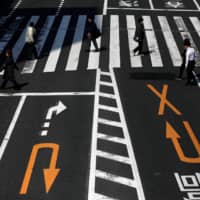 Fewer than usual pedestrians cross the street in Tokyo on Wednesday after the government announced the state of emergency in the capital amid the growing spread of COVID-19 in Japan. | REUTERS