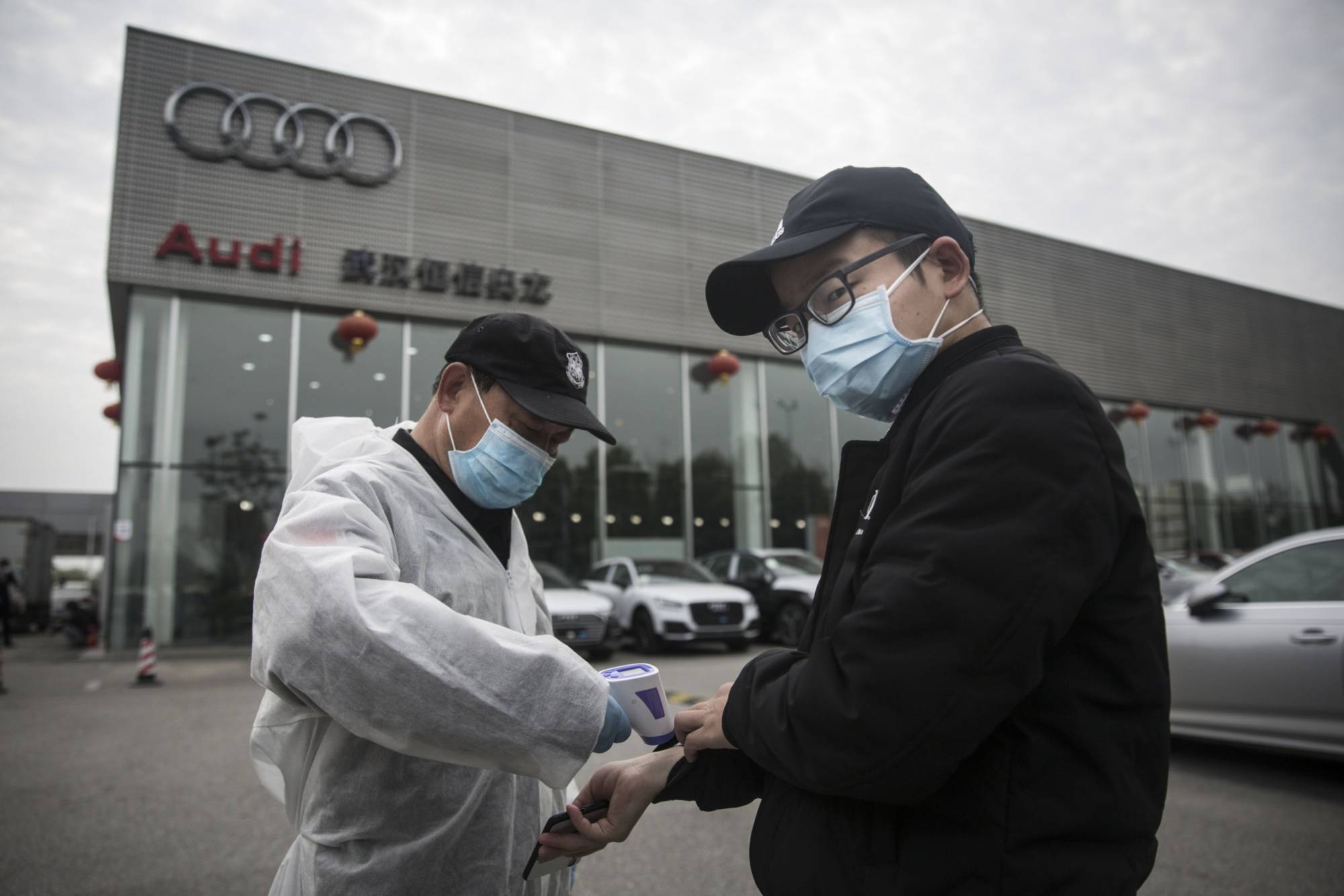 A security guard wears protective clothing as he checks the temperature of people entering the Audi store in Wuhan on Monday. | BLOOMBERG