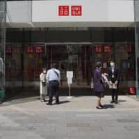 Employees speak to customers about a temporary closure due the coronavirus at a Uniqlo store, operated by Fast Retailing Co., in Ginza shopping district in Tokyo on Wednesday. | BLOOMBERG