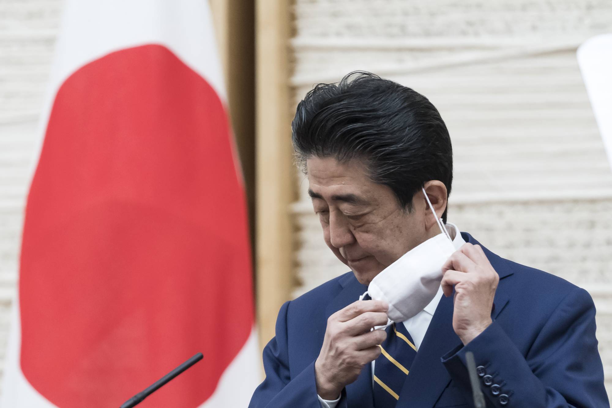 Prime Minister Shinzo Abe removes his mask during a news conference at the Prime Minister's Office on Tuesday after declaring a state of emergency for Tokyo and six other prefectures to contain the spread of the novel coronavirus. | AP