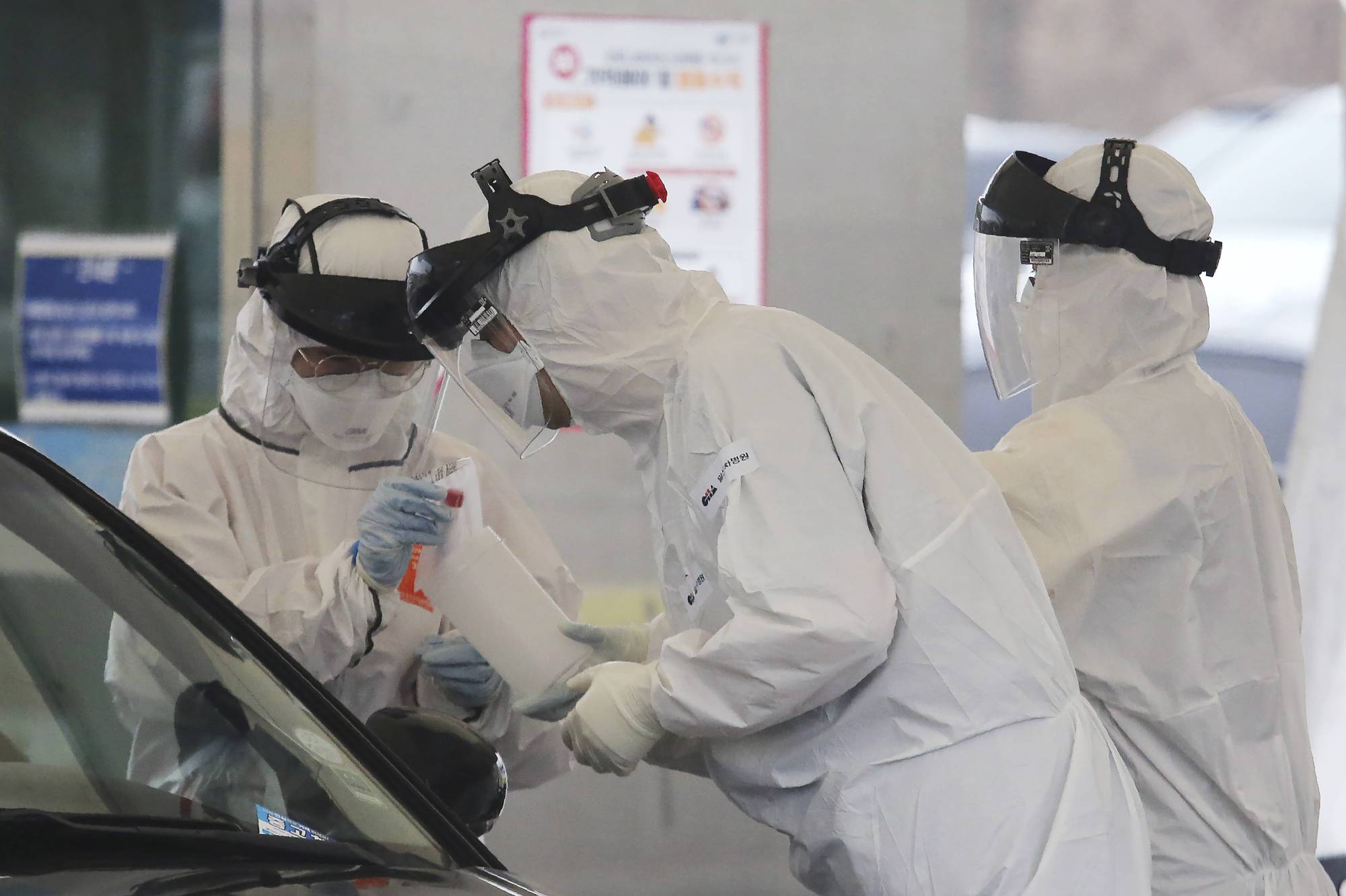 Medical staff wearing protective suits take samples from a person with suspected symptoms of the new coronavirus at a drive-thru test facility in Goyang, South Korea, last month. Officials on Friday reported that 91 patients in the country thought to have recovered from the new coronavirus had tested positive again. | AP