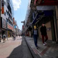 People wearing facemasks as a preventive measure against the COVID-19 coronavirus walk on a street of closed shops at shopping district Ameya-Yokocho, located next to Ueno Station, in Tokyo on Saturday. | AFP/JIJI