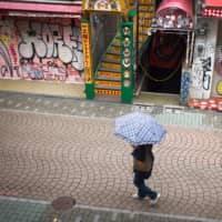 A pedestrian walks past shuttered stores in the Harajuku district of Tokyo on Sunday. | BLOOMBERG