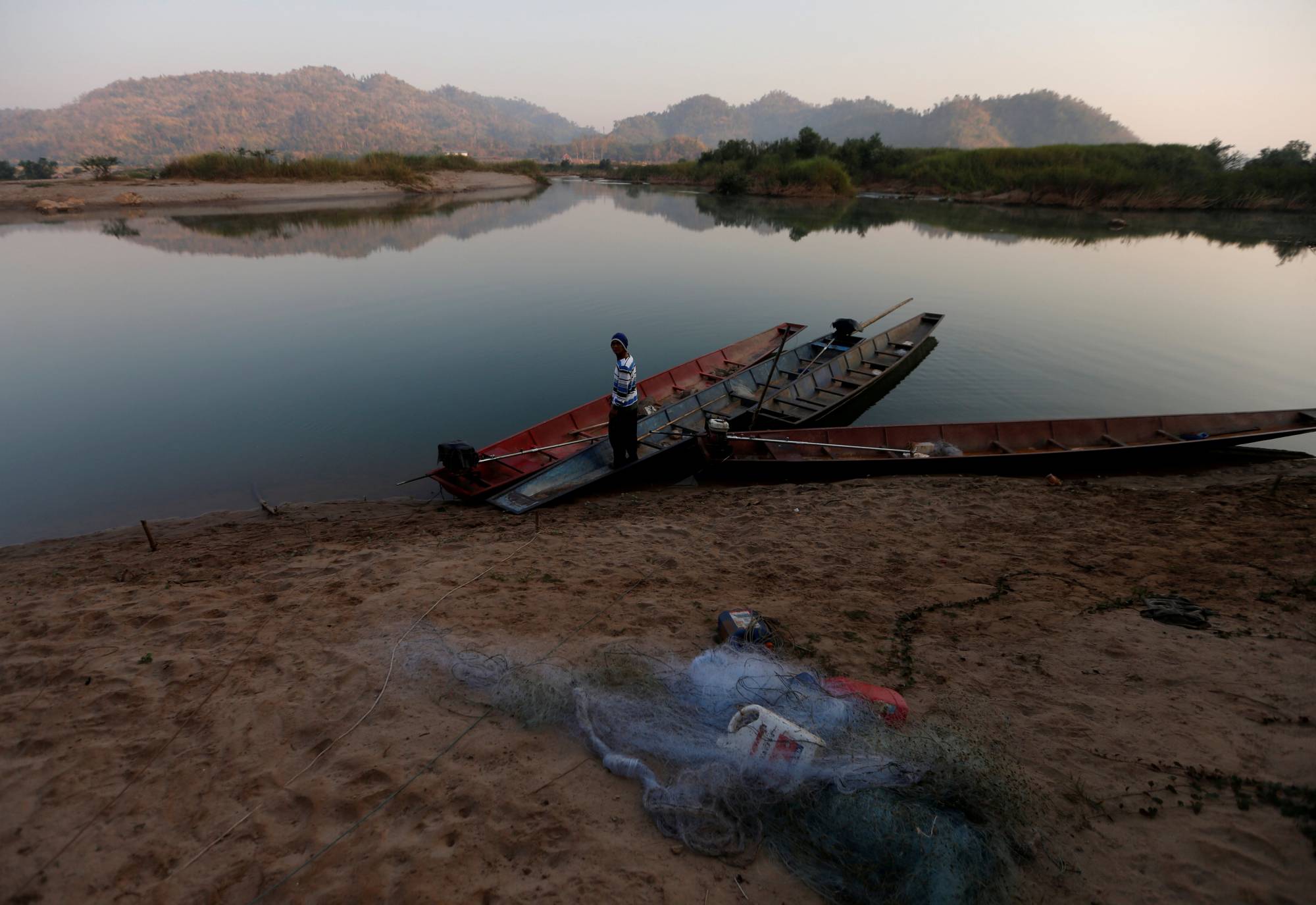 A fisherman stands in his boat on the Mekong riverbank outside Nong Khai, Thailand, in January. | REUTERS