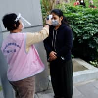 A masked local resident has her temperature checked as people line up to buy face masks from vending machines at the Xinyi District Health Center in Taipei on Tuesday. | AFP-JIJI